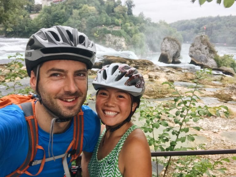 anya and phil smiling at the camera with rhine falls in the background. They're cycling the Eurovelo 15