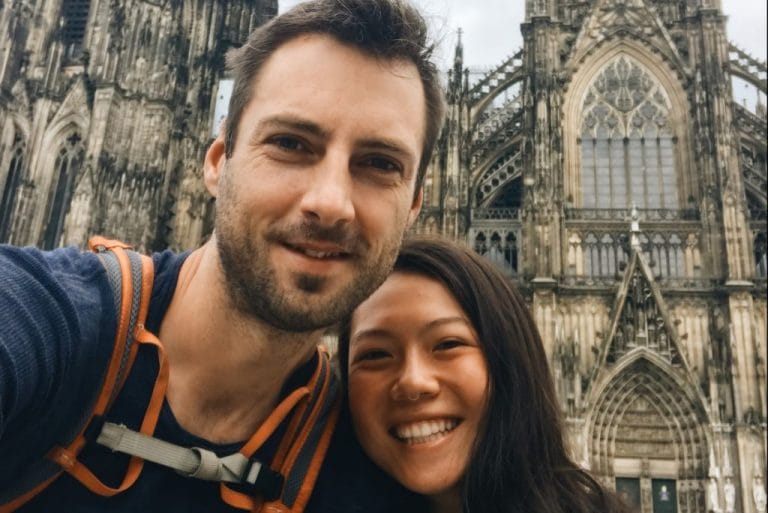 anya and phil smiling at the camera with the cologne cathedral behind them. Cologne was a stop on the Eurovelo 15. 