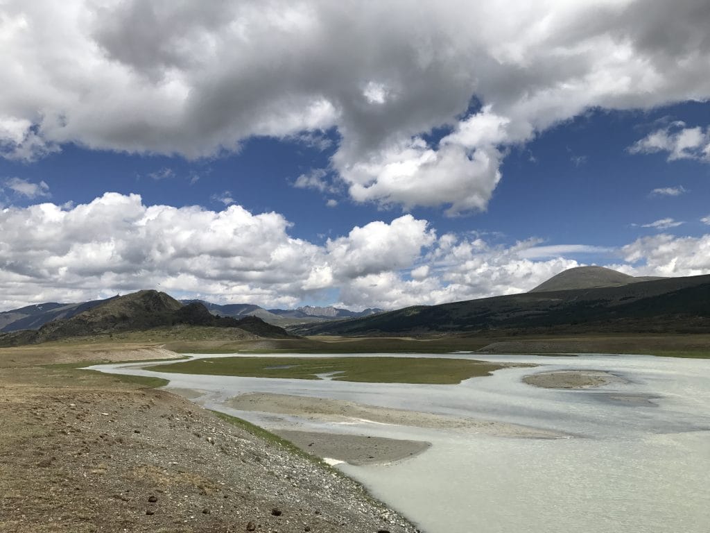 blue skies with clouds above a barren, half dried river
